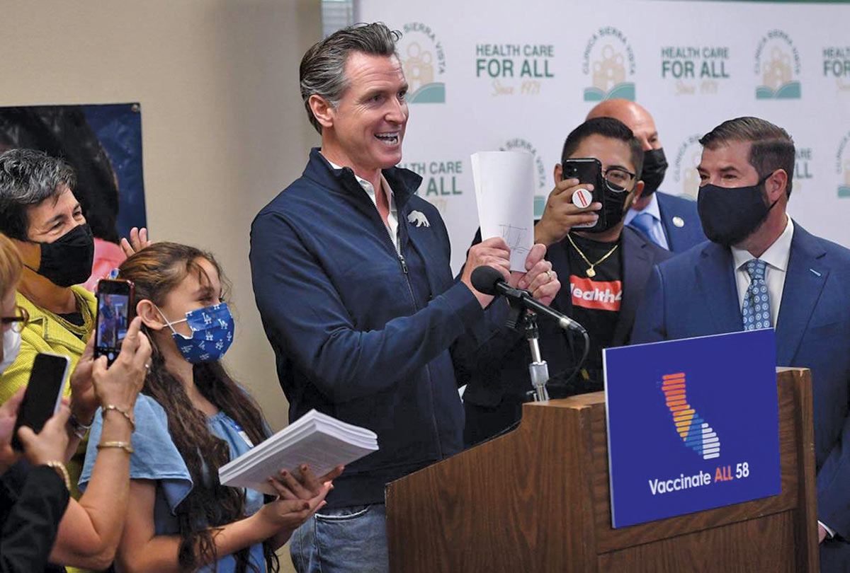 Gavin Newsom holds up paperwork for a bill expanding medical coverage for undocumented Caifornians—a position he’s since walked back.