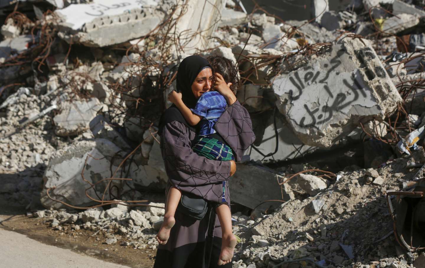 A Palestinian woman carrying her child in her arms cries in front of a building destroyed in Israel's attack on the Bureij Refugee Camp on September 19, 2024.