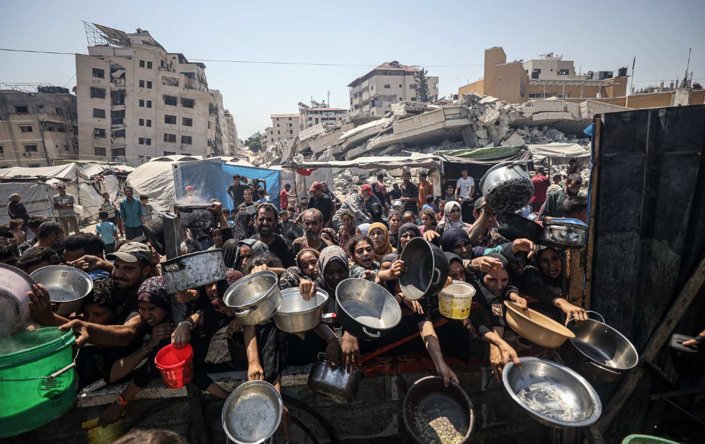Palestinians carrying pans, gather to receive hot meals, distributed by a charity organization