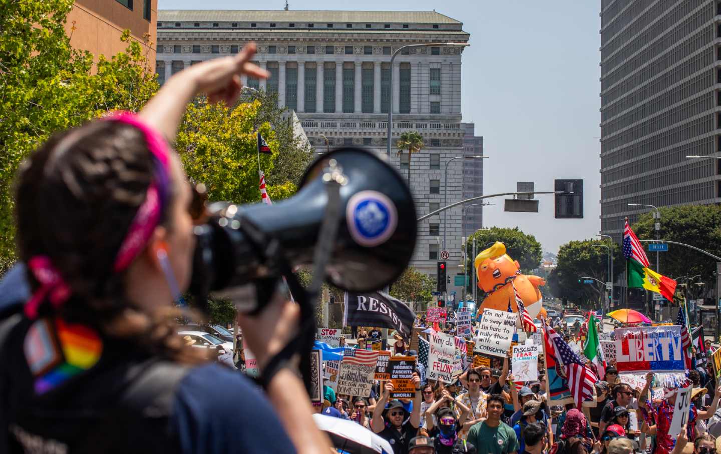 Protesters chant in Los Angeles while a Trump balloon flies over crowd.